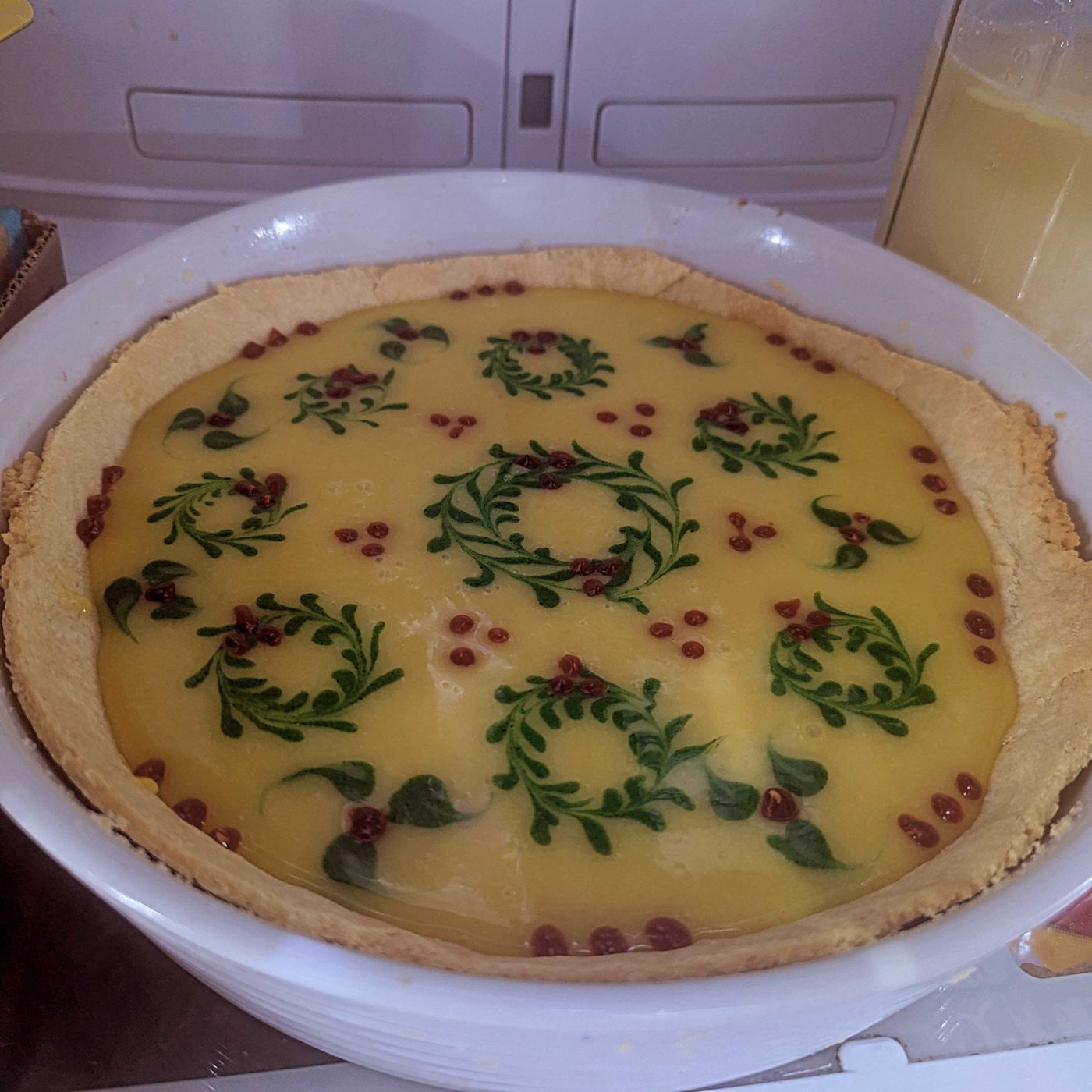 Custard tart decorated with piped green wreaths and berries